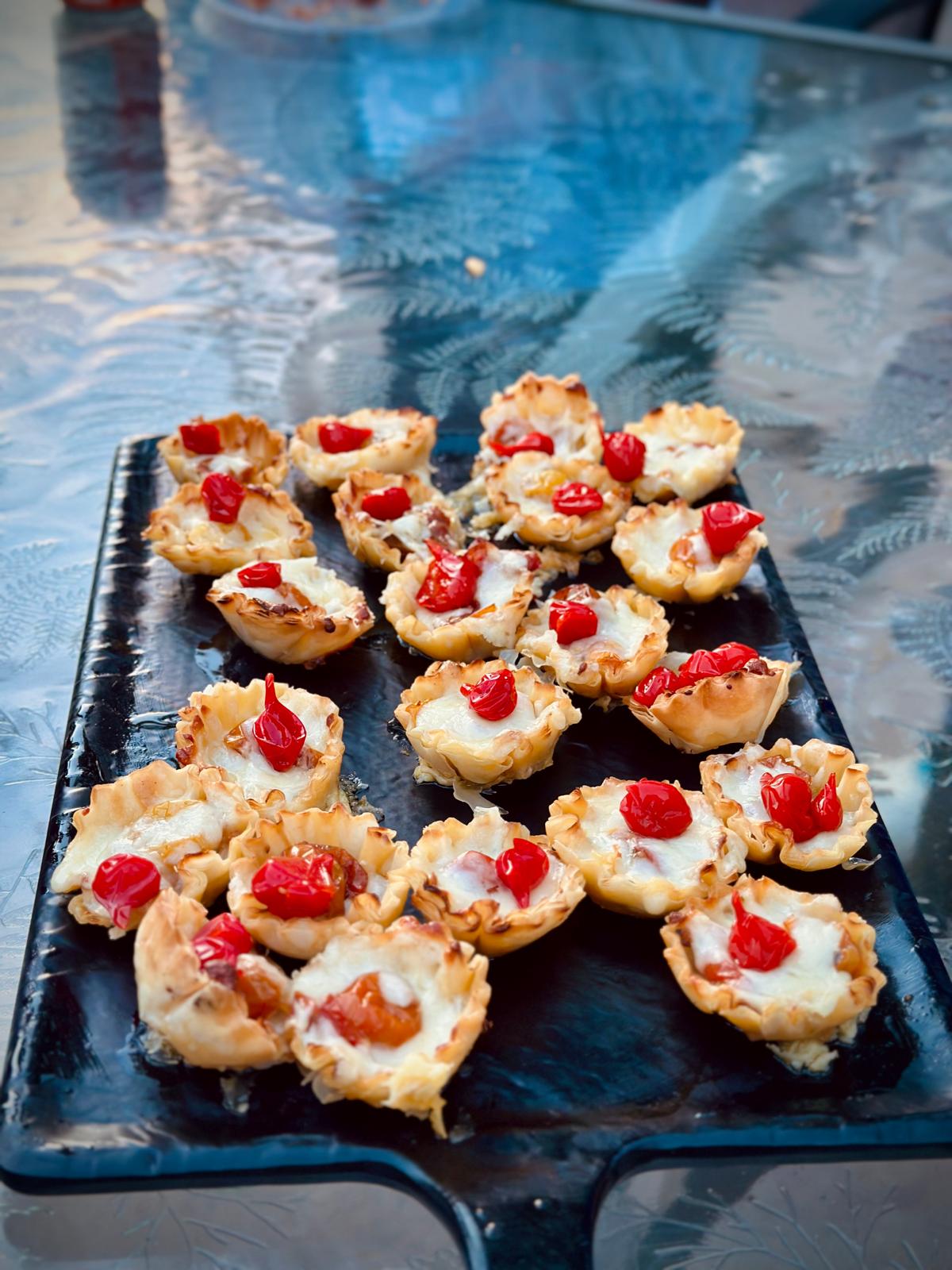 Bite-size phyllo cup appetizers topped with melted cheese and peppers