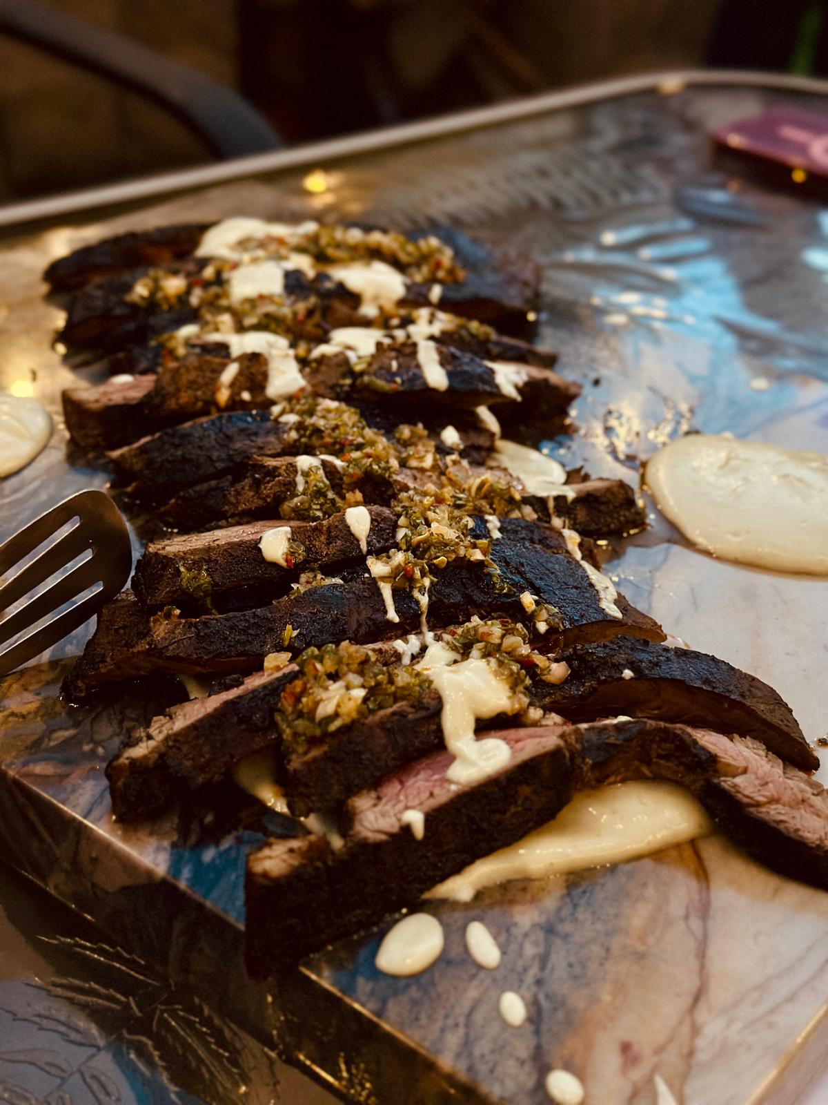 Sliced smoked steak drizzled with sauce and chimichurri on a serving tray